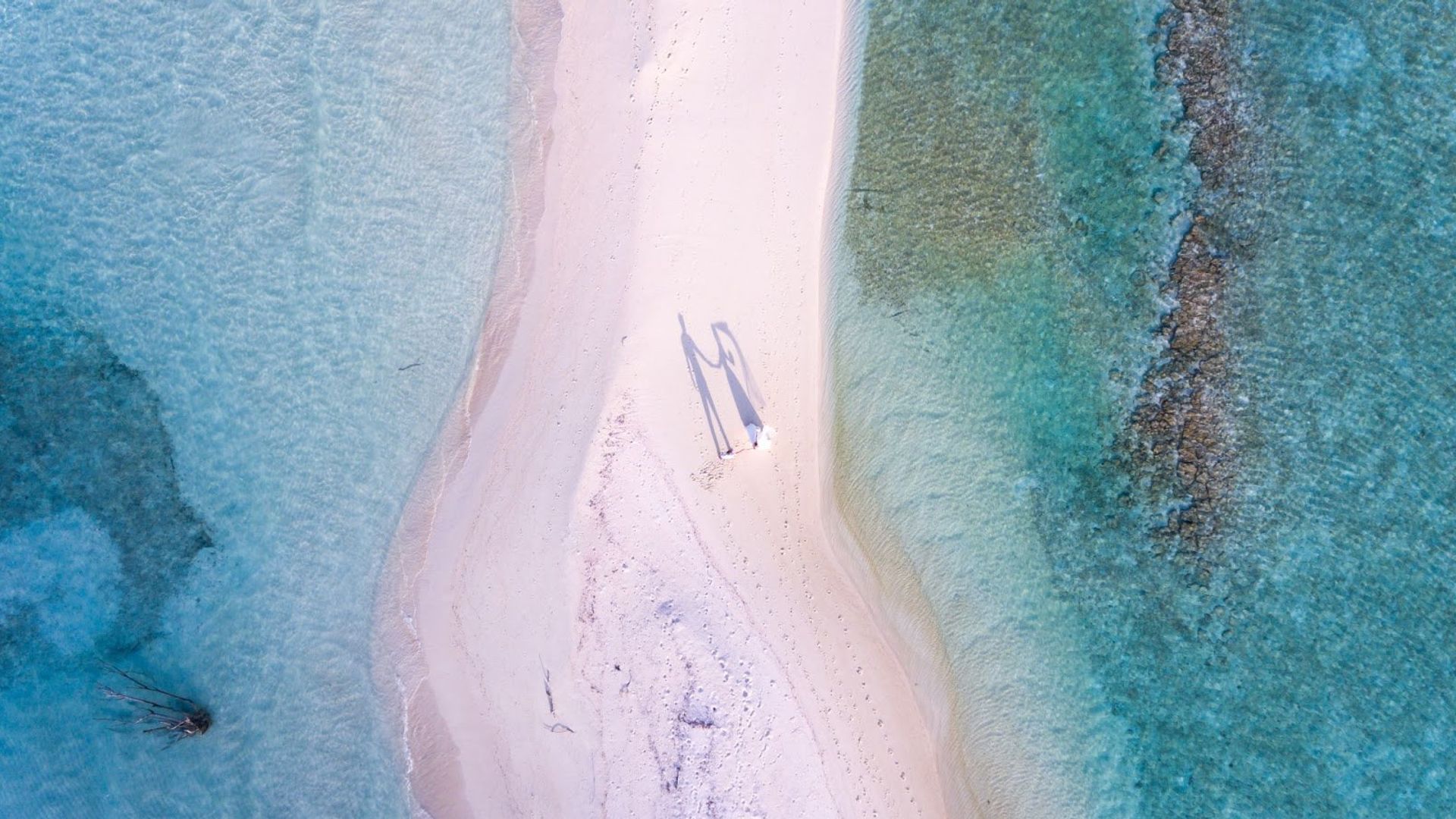 Aerial view of a couple standing on a sandbar surrounded by turquoise water in Hawaii