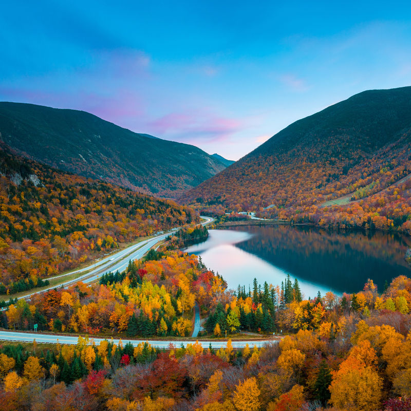 Autumnal foliage around a lake and road in New England, USA