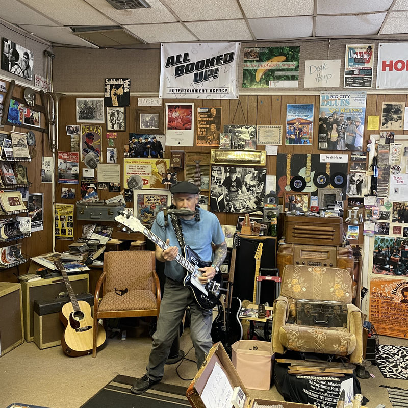 Een man speelt gitaar in zijn muziekstudio vol posters van muzikanten