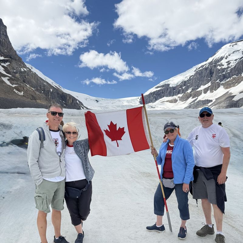 Four people standing in front of the Athabasca Glacier with a Canadian flag