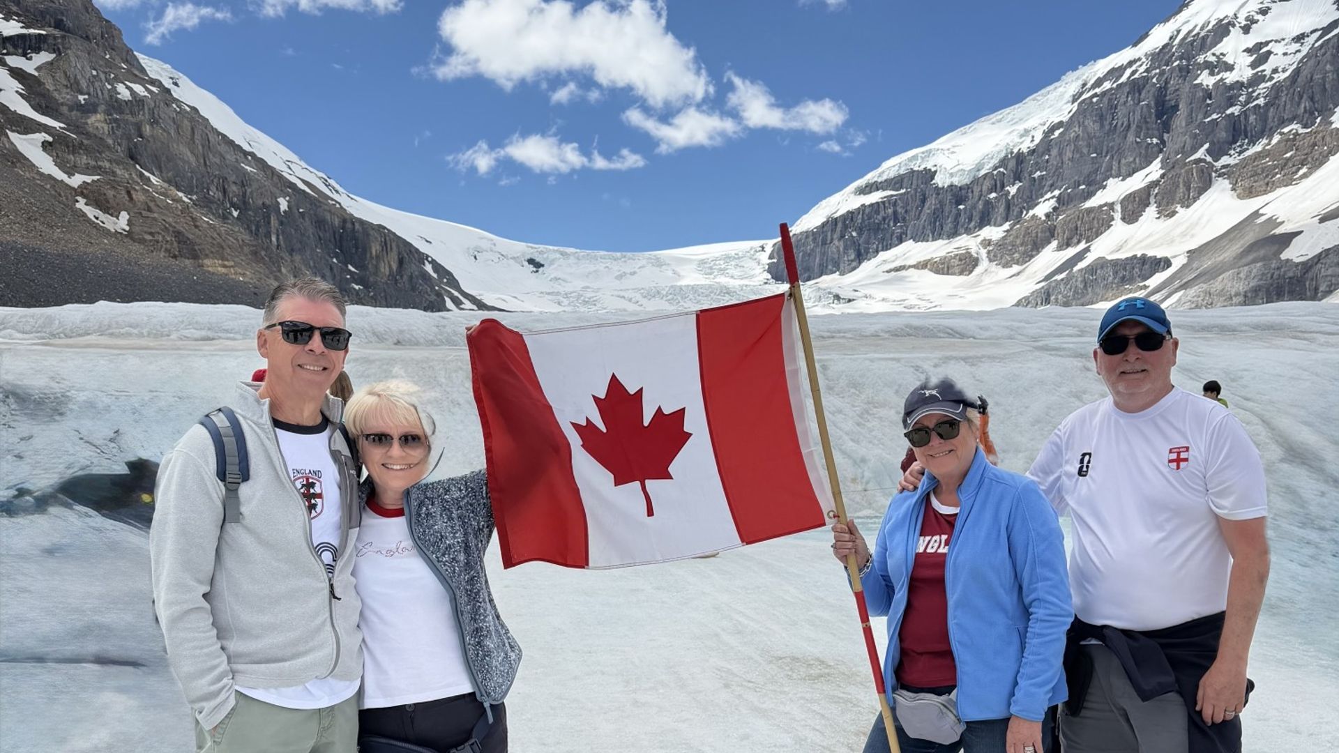 Four people standing in front of the Athabasca Glacier with a Canadian flag
