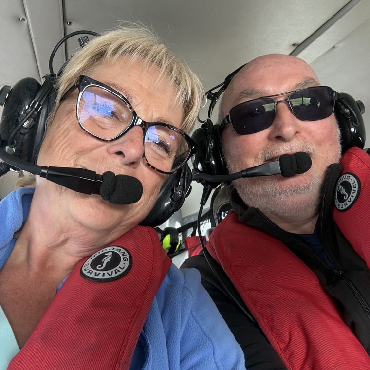 Customers taking a selfie wearing headsets and life vests during a helicopter tour