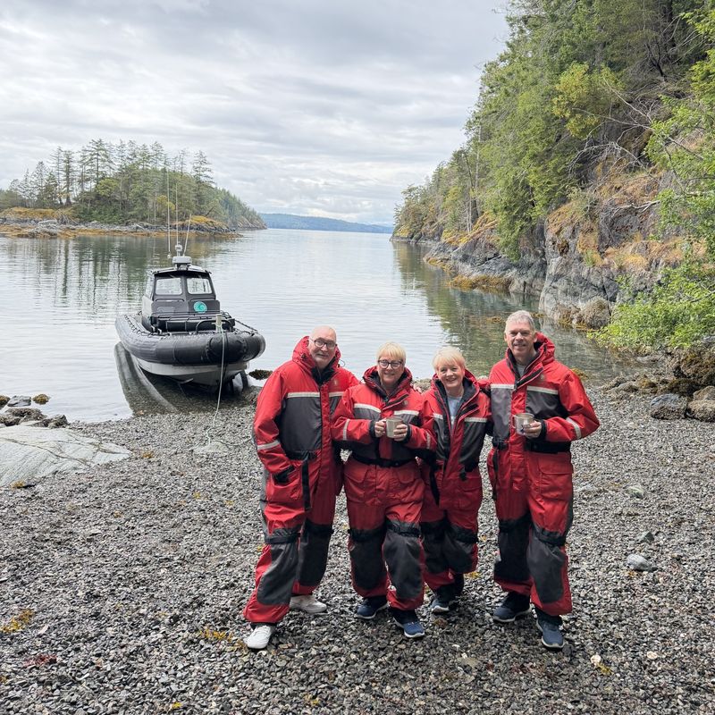 Four people with whale watching boat and pebble beach shore line behind them