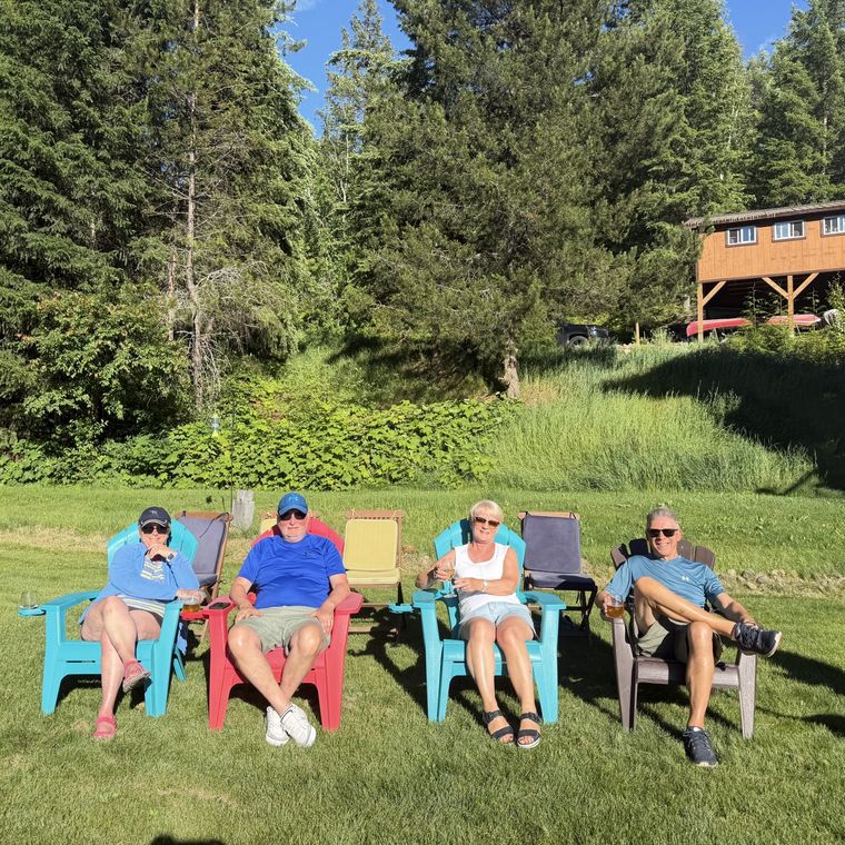 Four friends sat on Muskoka chairs with forrest and a log cabin behind them