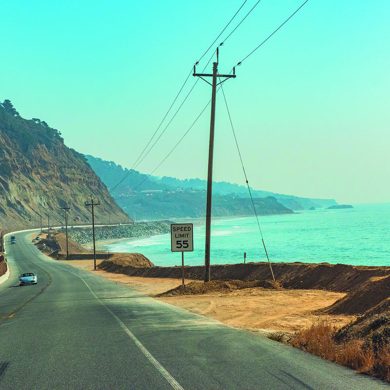 Een kustweg in Californië die buigt langs steile kliffen boven de oceaan, met auto's die langs het turquoise water rijden.