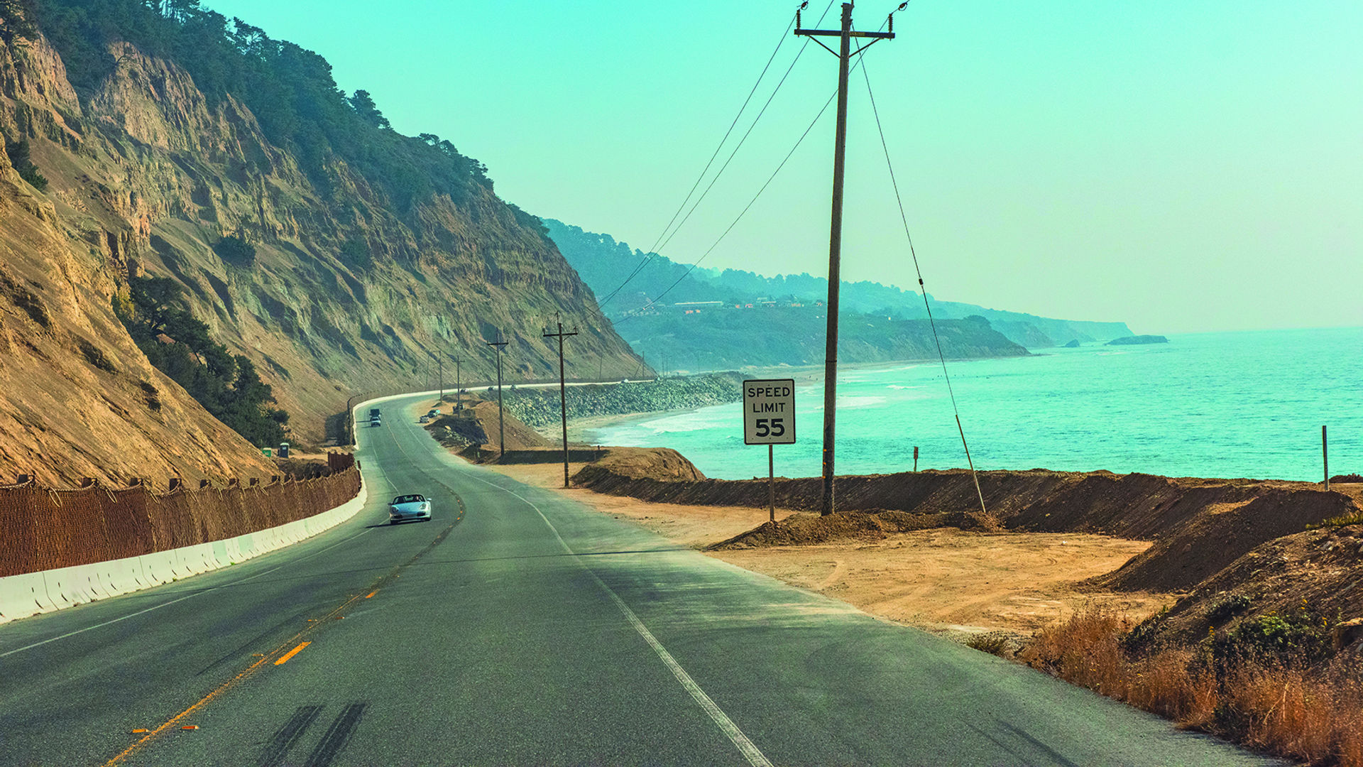 Een kustweg in Californië die buigt langs steile kliffen boven de oceaan, met auto's die langs het turquoise water rijden.