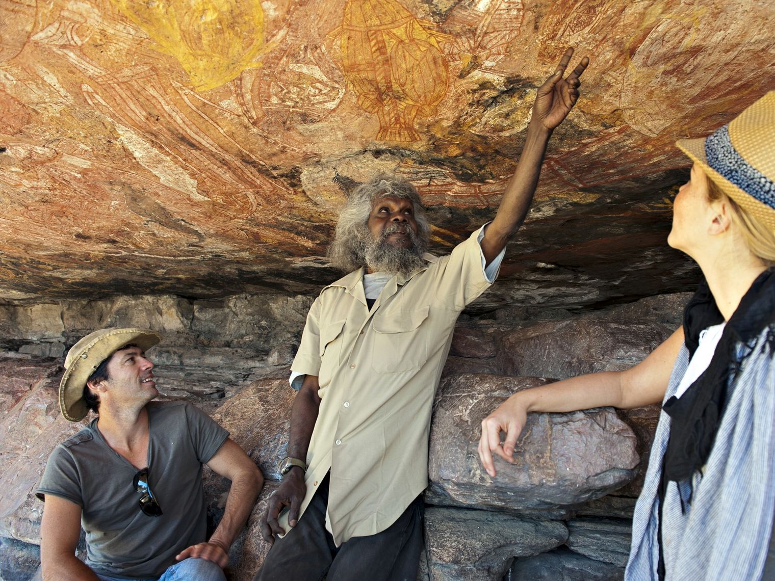 A local Aboriginal guide showing a pair of tourists ancient rock art in Australia