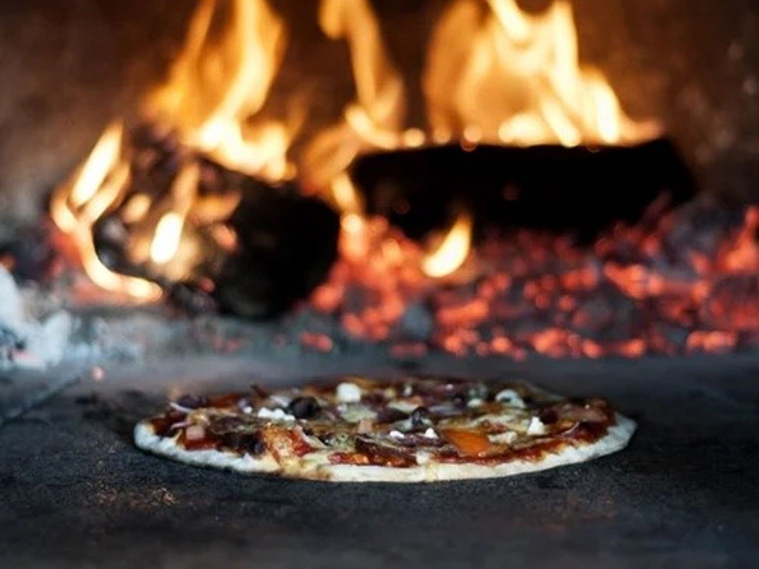 A pizza baking inside a wood fired oven