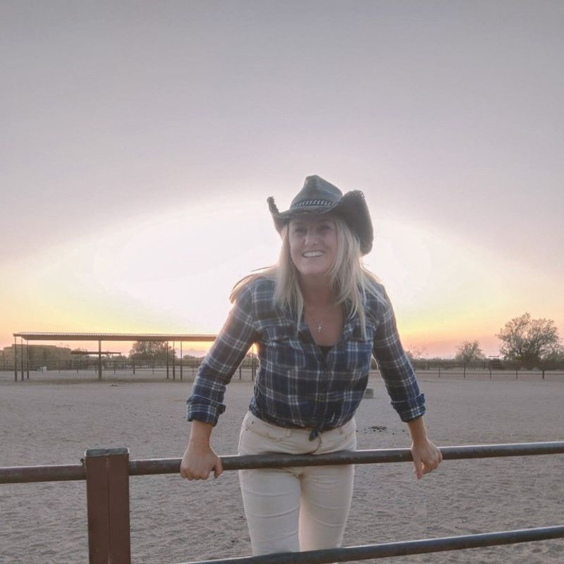 Vrouw met een cowboyhoed, die op een hek leunt.