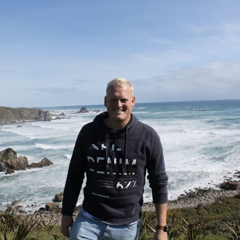 Maurits glimlacht naar de camera met de oceaan op de achtergrond