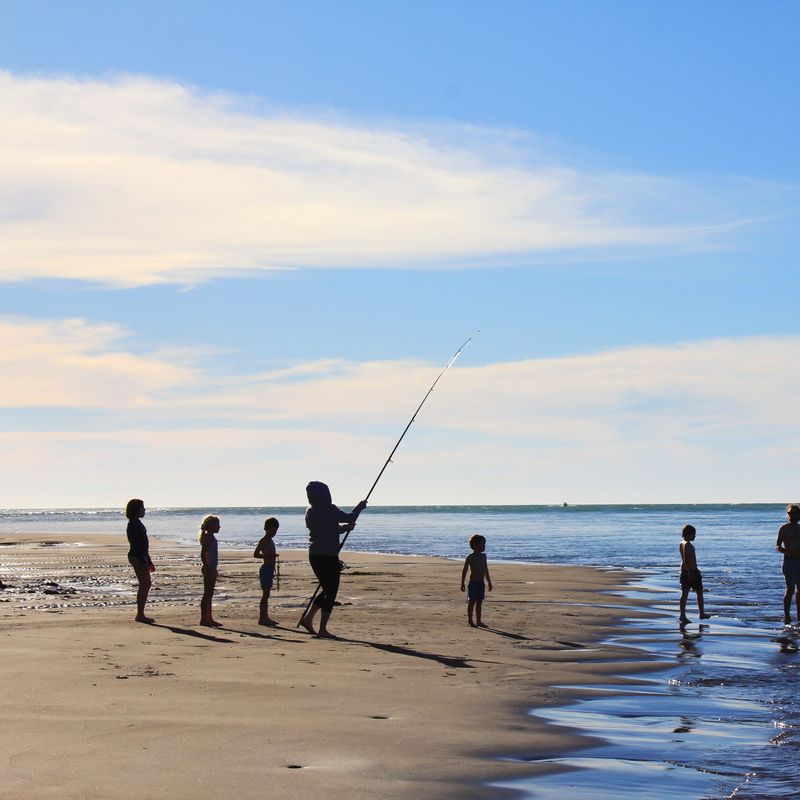 Personen stehen an Strand und angeln in Neuseeland