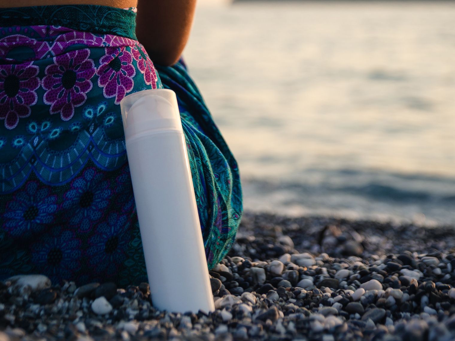 Frau von hinten, die auf Kieselstrand und Gewässer sitzt mit einer Sprayflasche an ihr gelehnt