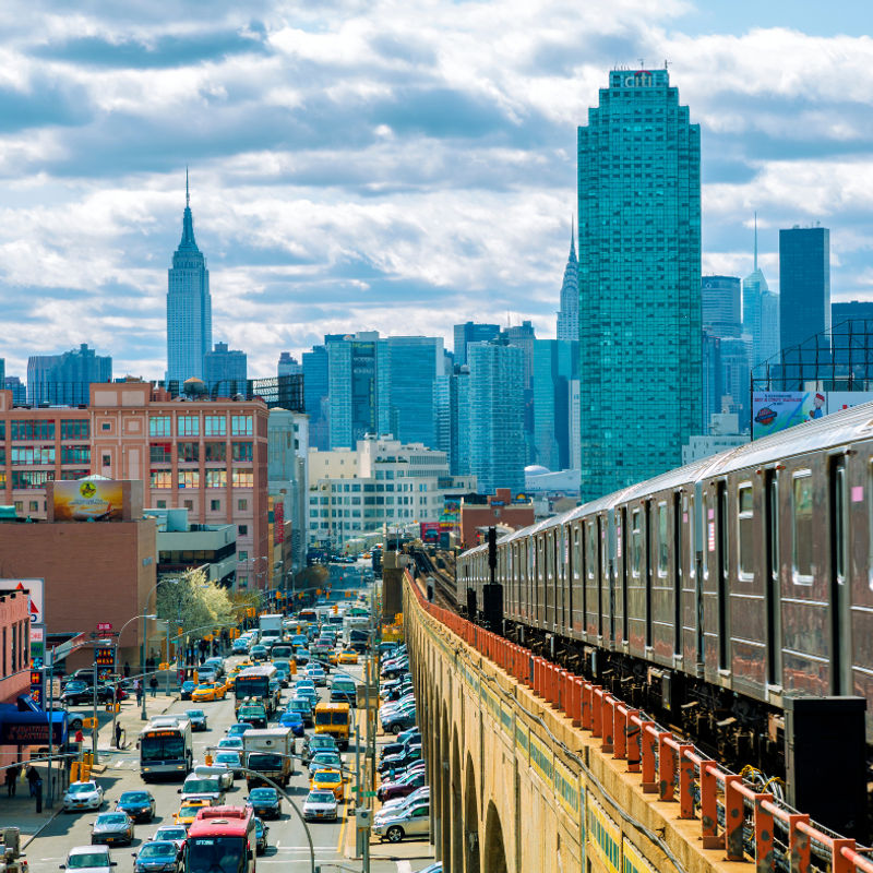 Een tram rijdt op een verhoogde brug met uitzicht op de skyline van Queens