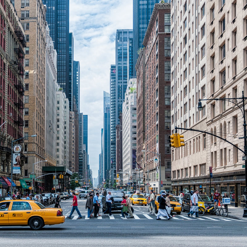 Een straat in New York, mensen steken een zebra over en er rijdt een gele taxi