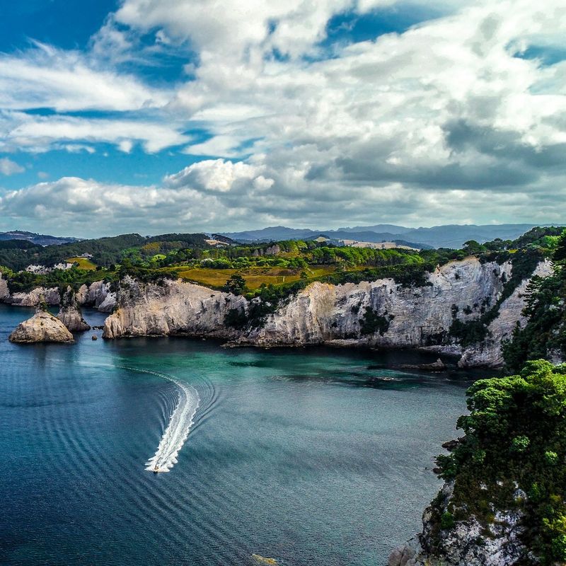 The rugged Coromandel Coastline with grey cliffs, blue waters and green fields