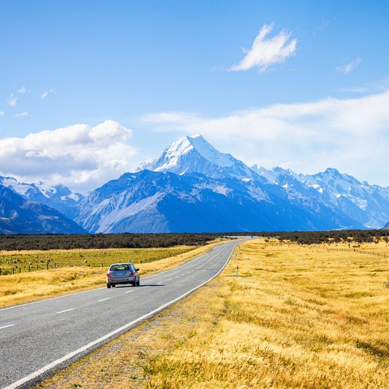 Ein Auto fährt auf einer geraden Straße auf verschneite Berggipfel in Neuseeland zu