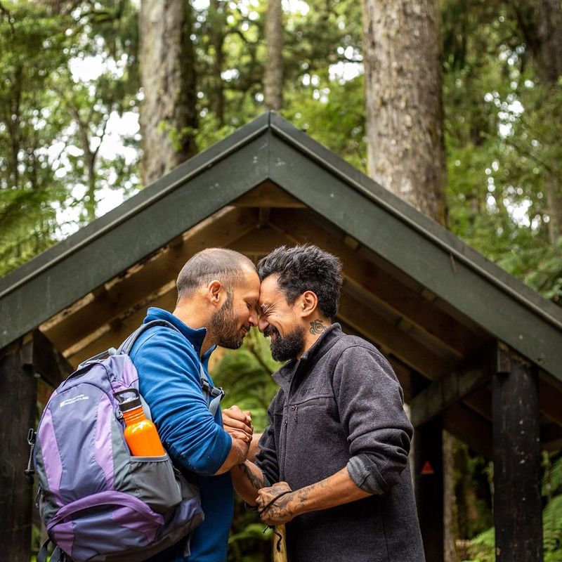 Twee mannen voeren een traditionele Māori-groet uit in een bosrijke omgeving.