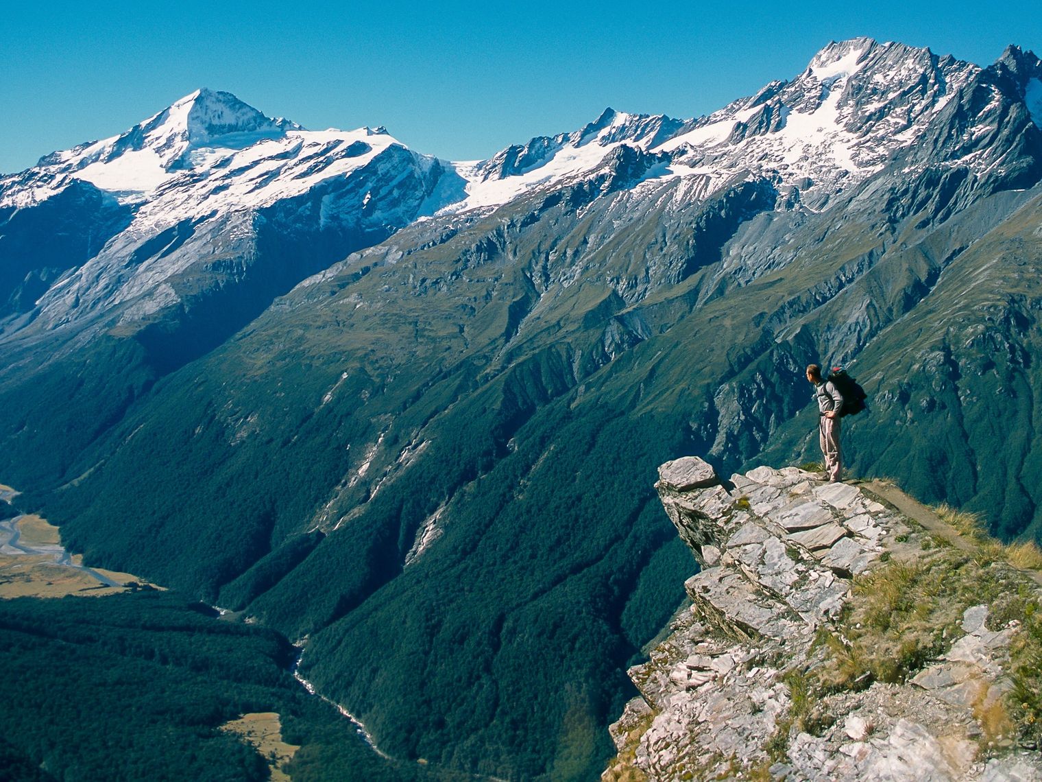 Wanderer steht auf Felsvorsprung mit schneebedeckten Bergen im Hintergrund
