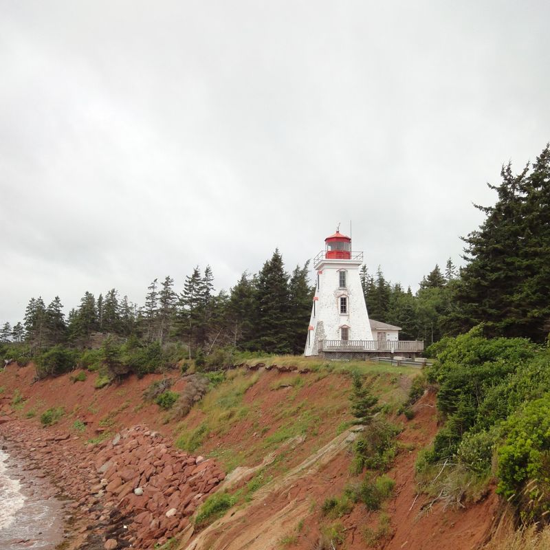 Rode kliffen van Cape Bear op Prince Edward Island, een vuurtoren staat aan de kust, omringd door groene bossen