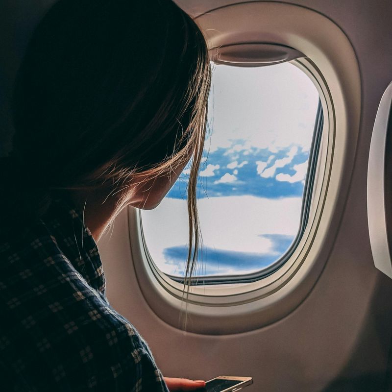 Passagier kijkt tijdens de vlucht uit het vliegtuigraam naar de wolken
