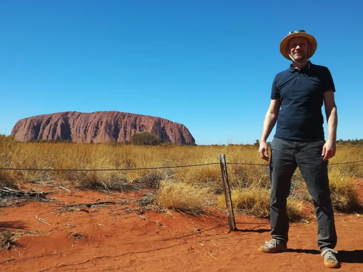 Mann steht auf rotem Sand vor dem Uluru in Australien