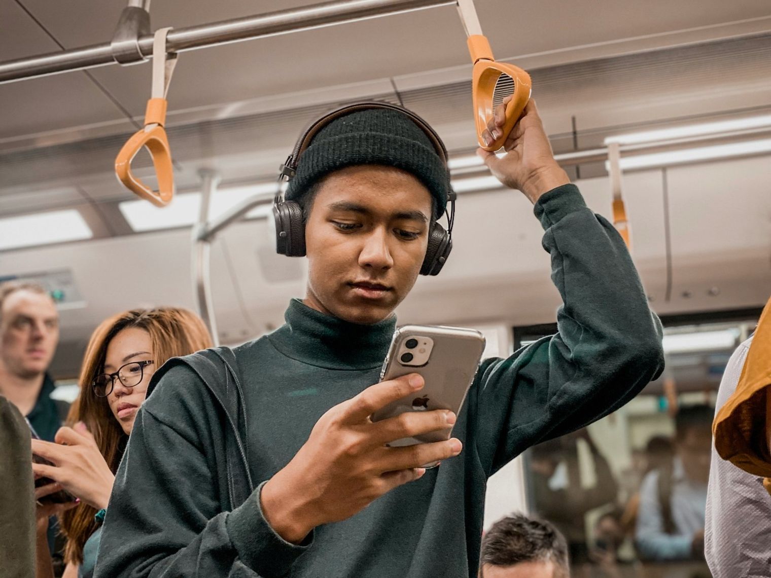 Ein Mann fährt im Zug, während er auf sein Handy schaut und Kopfhörer trägt