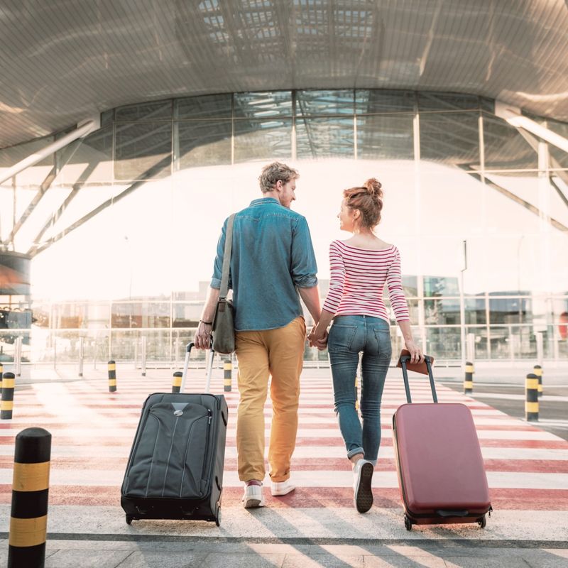 Ein Pärchen mit Ziehkoffern hält Händchen und läuft in Flughafen