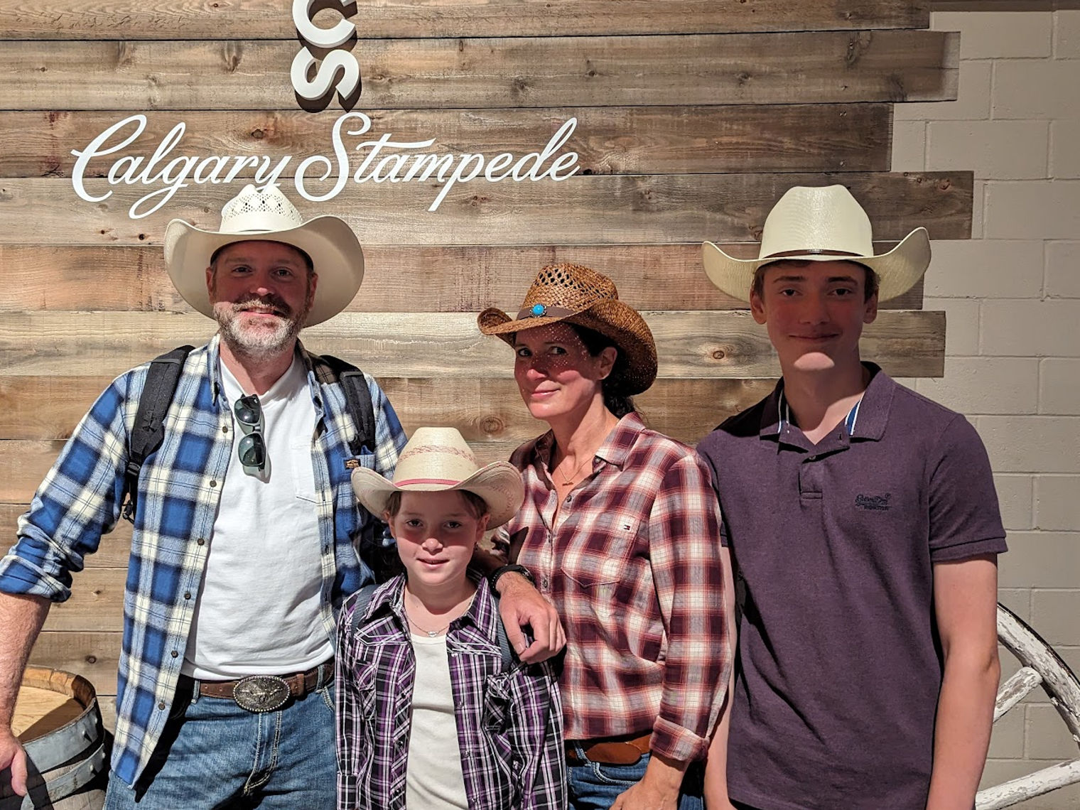 Familie mit zwei Kindern trägt Cowboyhüte und posiert vor Holzwand auf der Calgary Stampede
