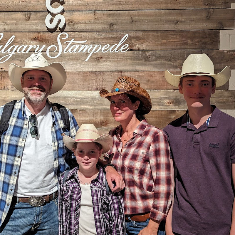 Familie mit zwei Kindern trägt Cowboyhüte und posiert vor Holzwand auf der Calgary Stampede