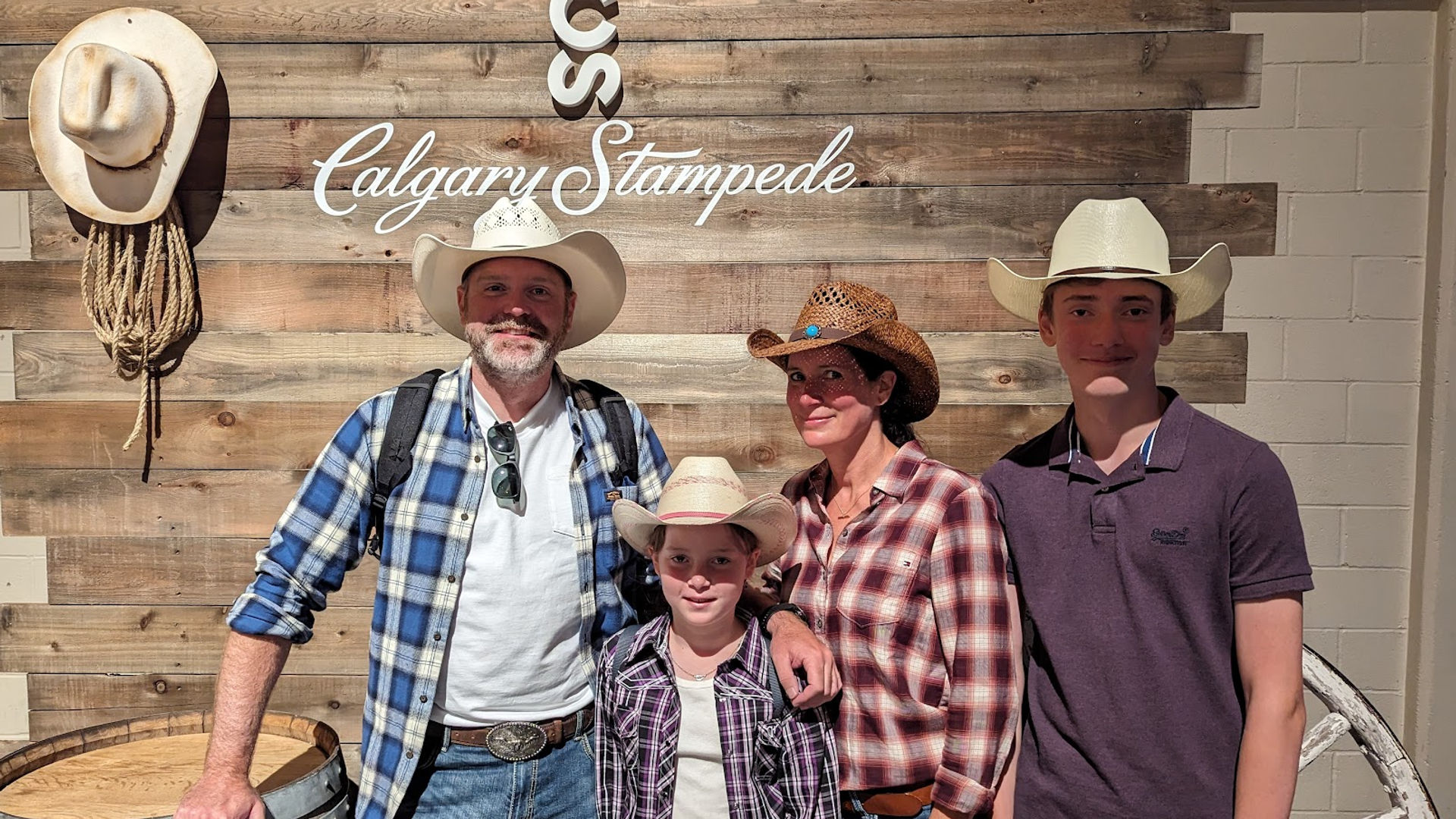 Familie mit zwei Kindern trägt Cowboyhüte und posiert vor Holzwand auf der Calgary Stampede