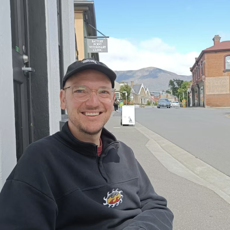 Sjoerd lacht naar de camera met een stad en bergen op de achtergrond