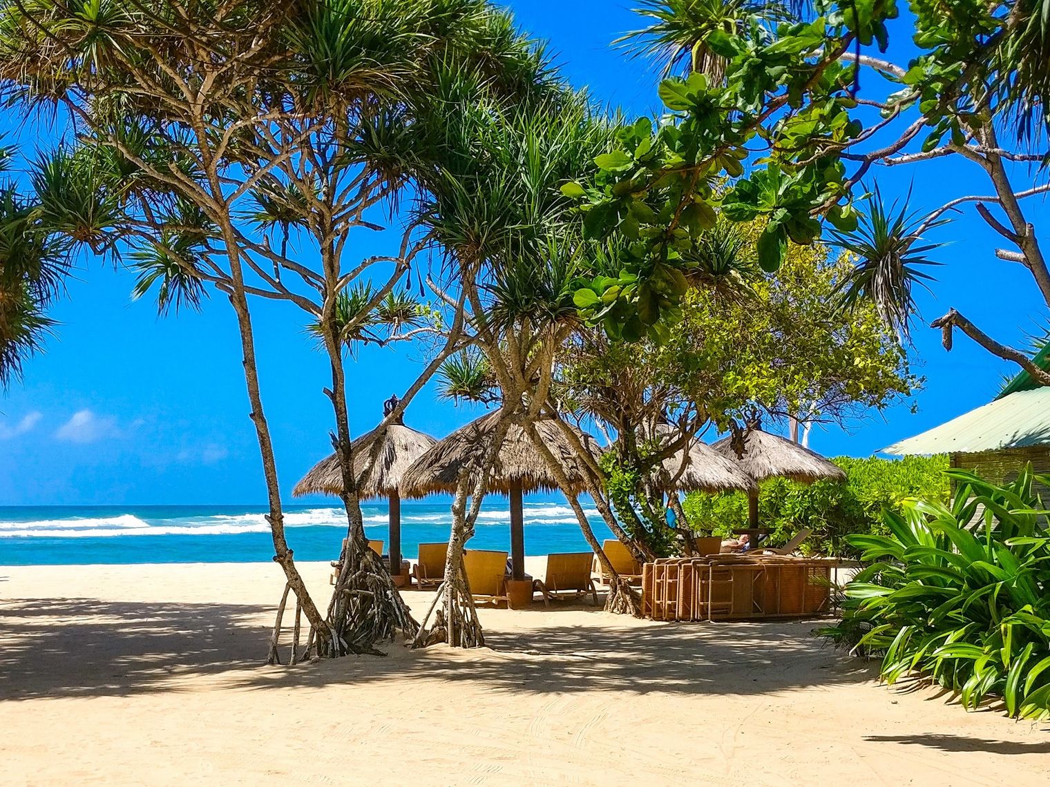 Beach with straw huts and seating areas looking out at the ocean in Bali