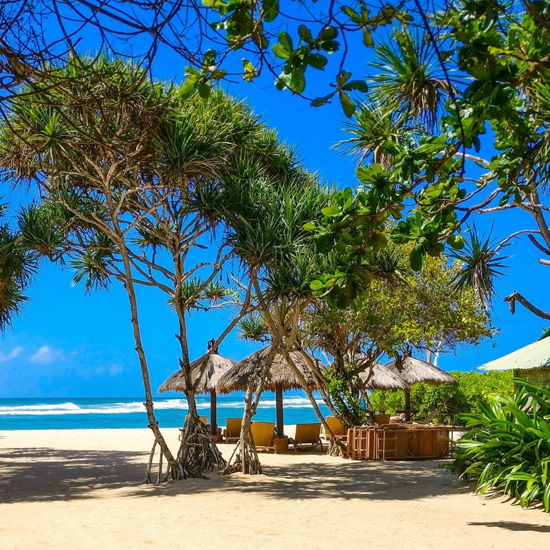 Strand mit Strohhütten und Sitzgelegenheiten mit Blick auf den Ozean in Bali