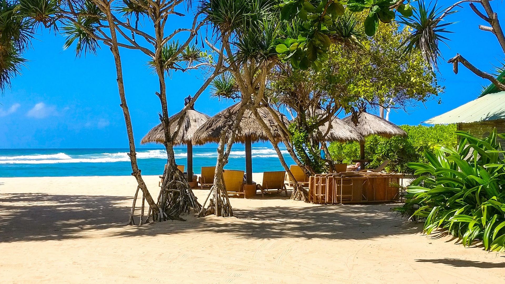 Strand mit Strohhütten und Sitzgelegenheiten mit Blick auf den Ozean in Bali