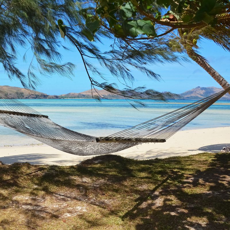 Een hangmat tussen twee bomen op het strand met de oceaan en andere eilanden op de achtergrond