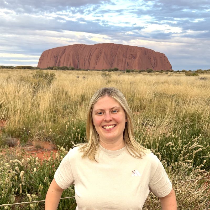 Blonde Frau steht tagsüber vor dem Uluru in Australien und lächelt