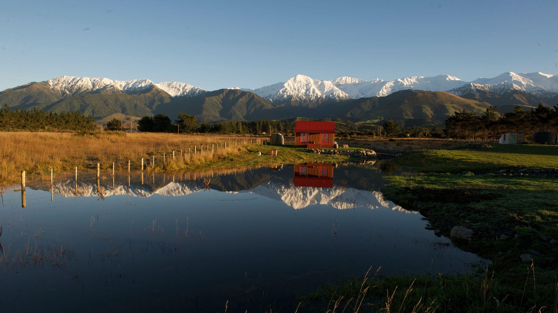 Een kleine accommodatie met besneeuwde bergen op de achtergrond weerspiegeld in het water, Kaikoura Nieuw-Zeeland