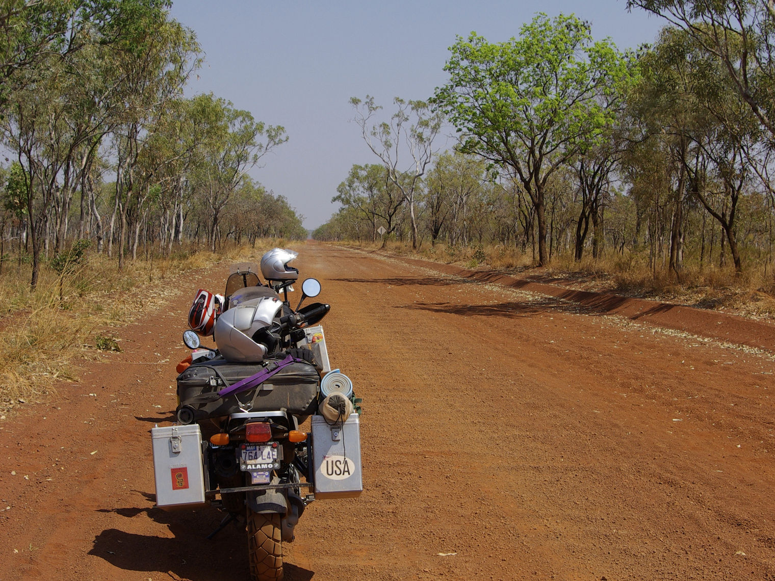 Loaded motorcycle riding on an unpaved red dirt road in the Australian outback