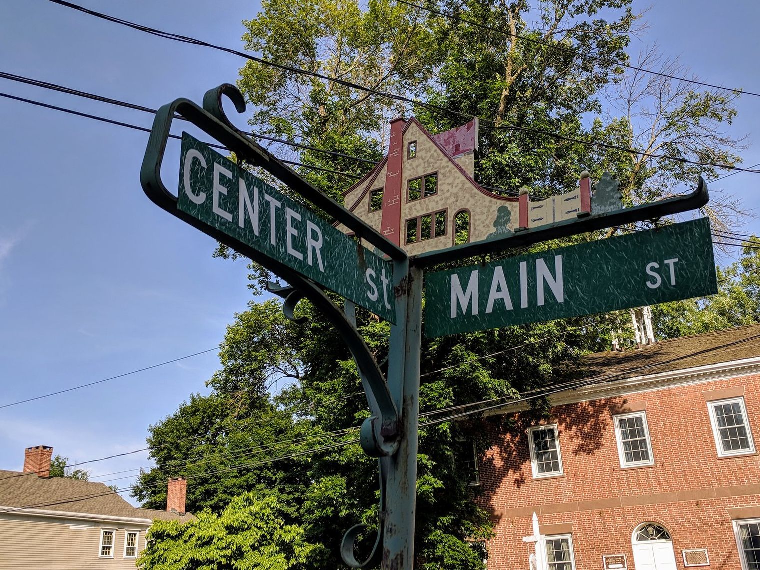 A vintage street sign marking the corner of Center Street and Main Street in a small American town, with historic brick buildings and trees in the background.