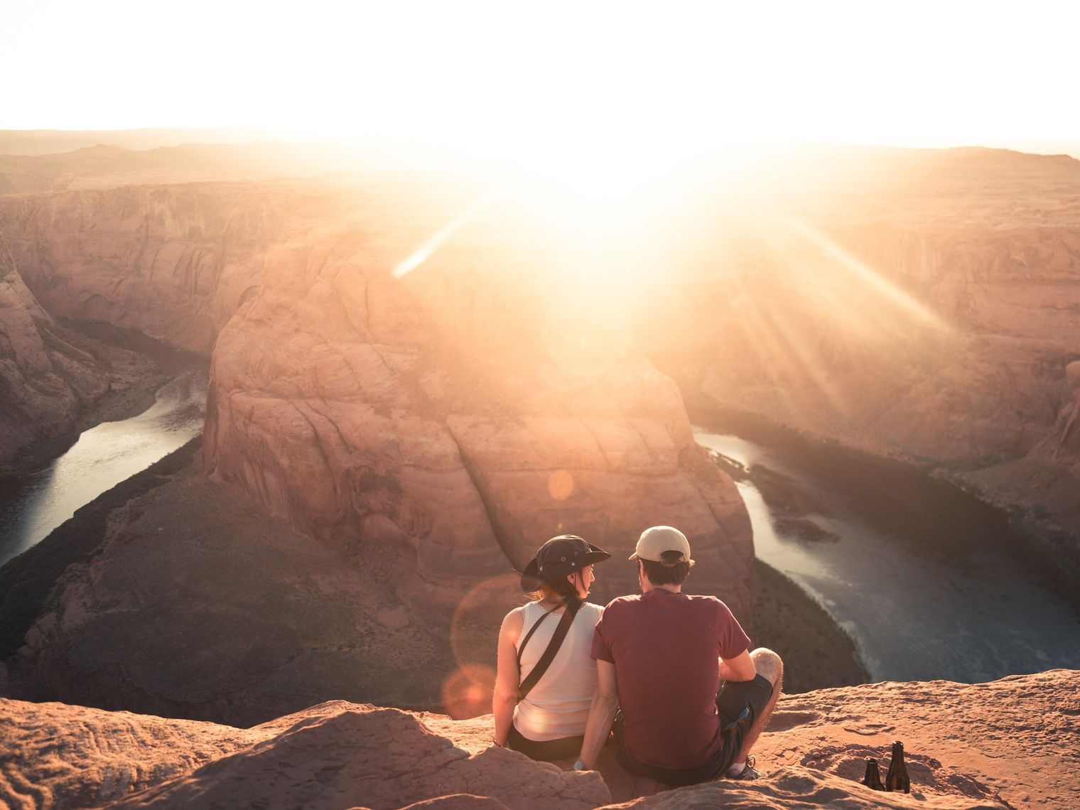 Ein Paar sitzt mit Blick auf Horseshoe Bend in Moab, Arizona, während die Sonne direkt in die Linse scheint.