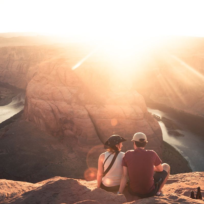 Een stel zit met uitzicht op Horseshoe Bend in Moab, Arizona, terwijl de zon fel in de lens schijnt.