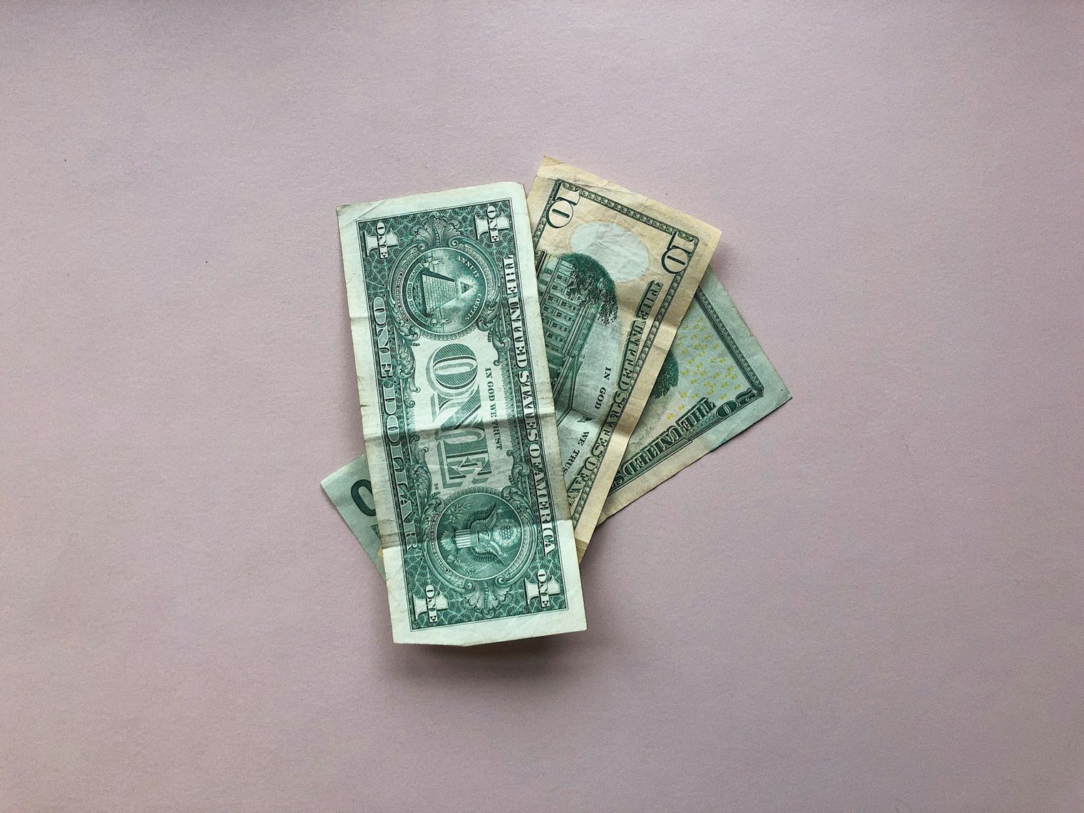 Ein kleiner Stapel von US-Dollarnoten liegt auf einer blassrosa Fläche.