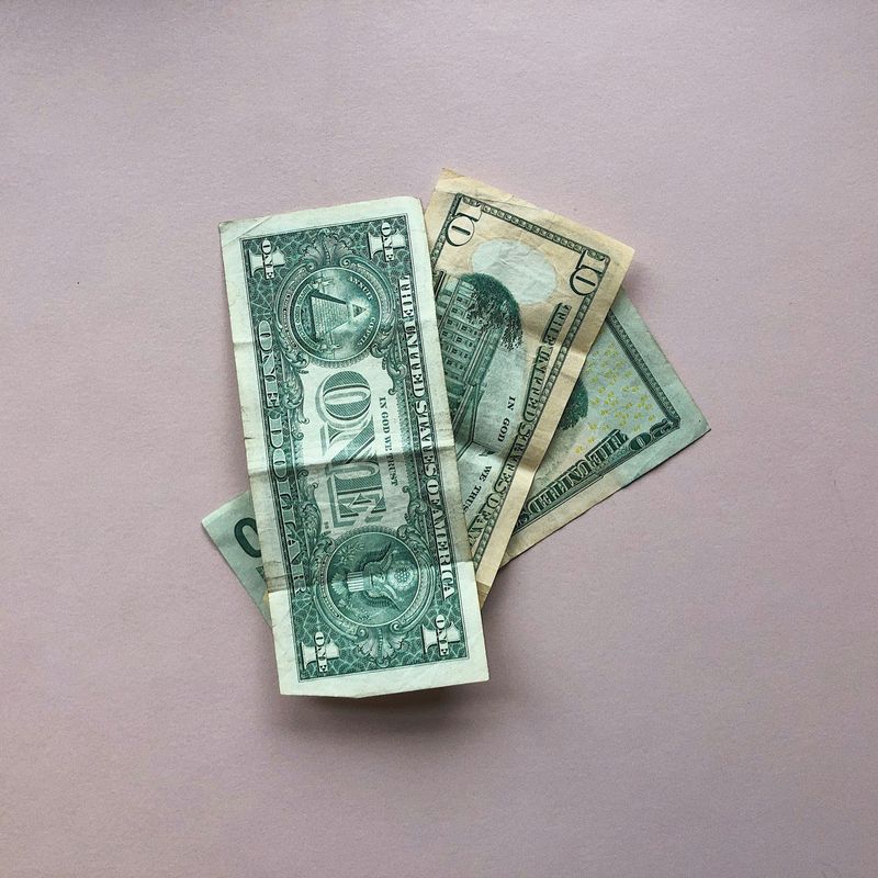 Een klein stapeltje Amerikaanse dollarbiljetten op een lichtroze oppervlak.