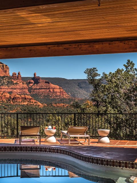 Private pool terrace with sun loungers under a timber roof, with sweeping views over the iconic red rock formations of Sedona, Arizona USA under a clear blue sky