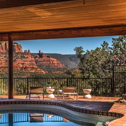 Private Poolterrasse mit Sonnenliegen unter einem Holzdach, mit weitem Blick über die ikonischen roten Felsformationen von Sedona, Arizona USA unter einem klaren blauen Himmel