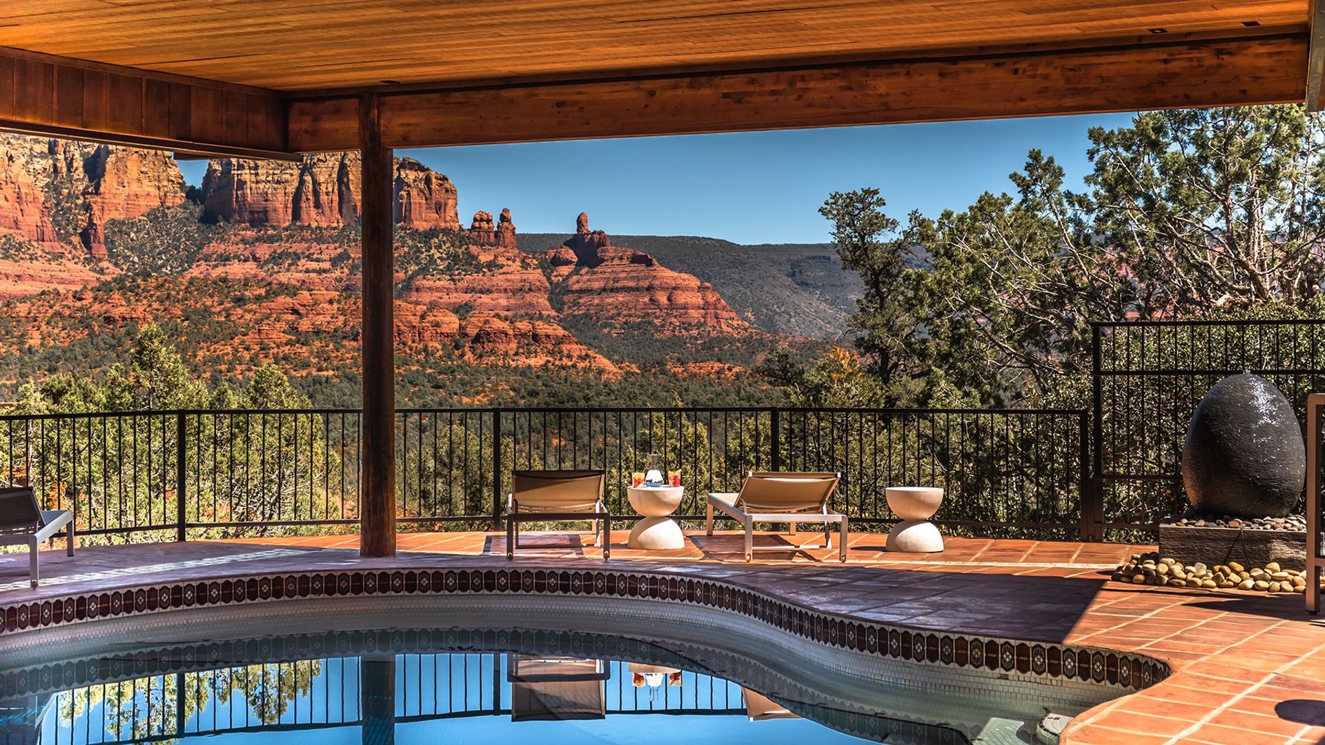 Privézwembadterras met ligstoelen onder een houten dak, met een prachtig uitzicht over de iconische rode rotsformaties van Sedona, Arizona, VS, onder een helderblauwe hemel.