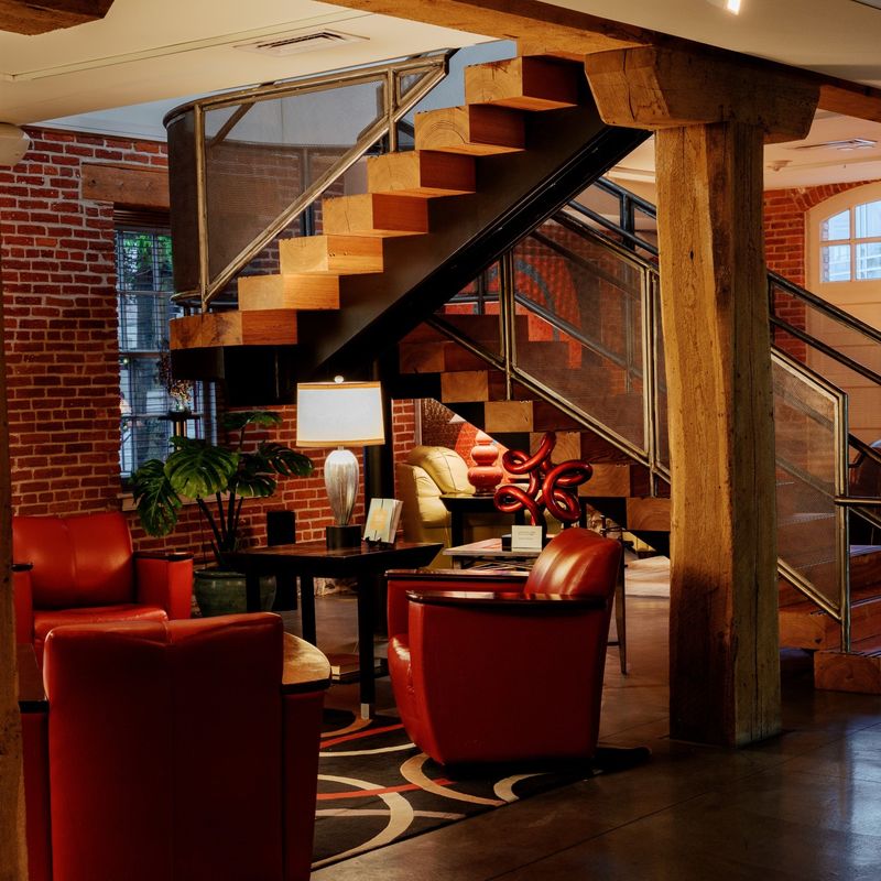 Stijlvolle lobby van een boetiekhotel in Pennsylvania, VS, met bakstenen muren, zware houten balken, rode leren fauteuils en een sculpturale zwevende trap in een gerenoveerd historisch gebouw.