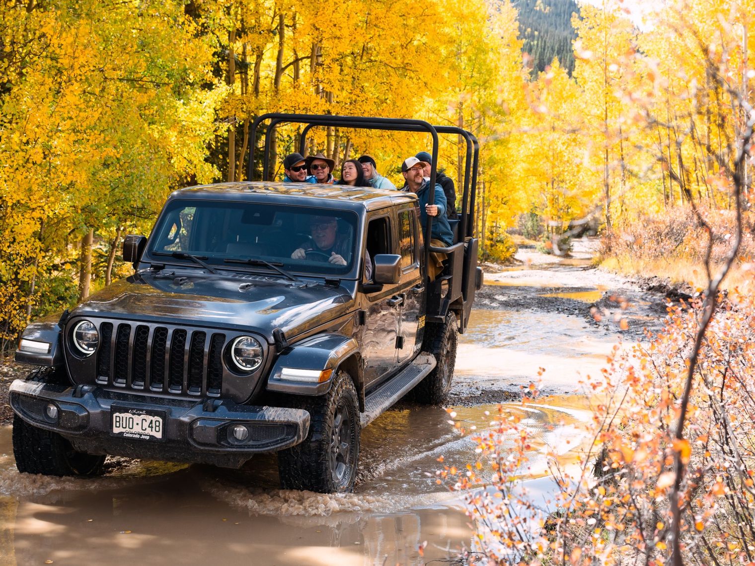 Ein Jeep mit Passagieren fährt durch eine teilweise geflutete Straße und einen herbstlichen Wald in Ouray, Colorado