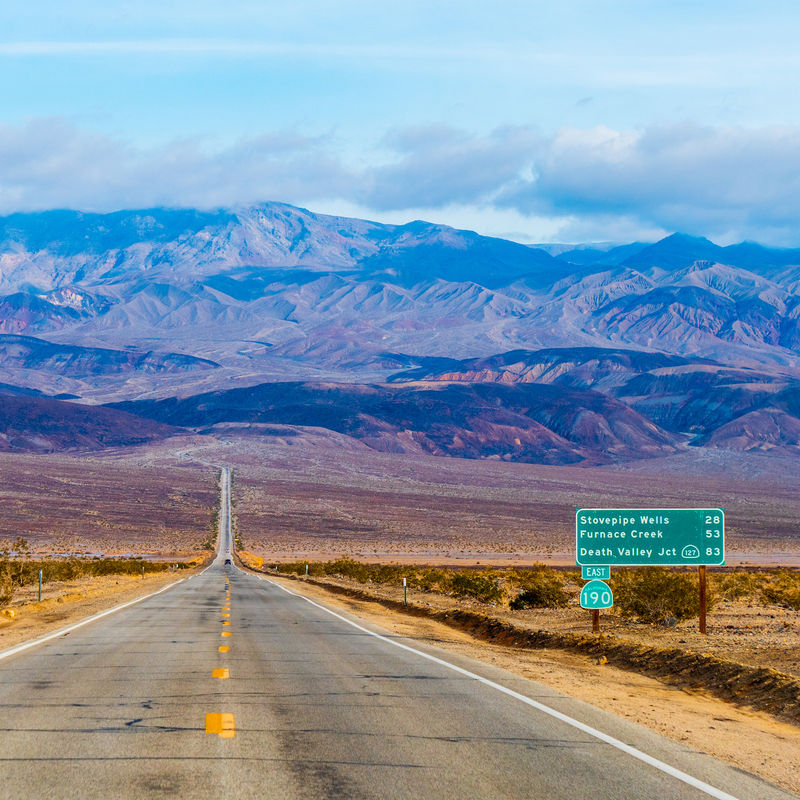 A long open road stretches out ahead with desert and mountains in the distance in the Mojave Desert, California