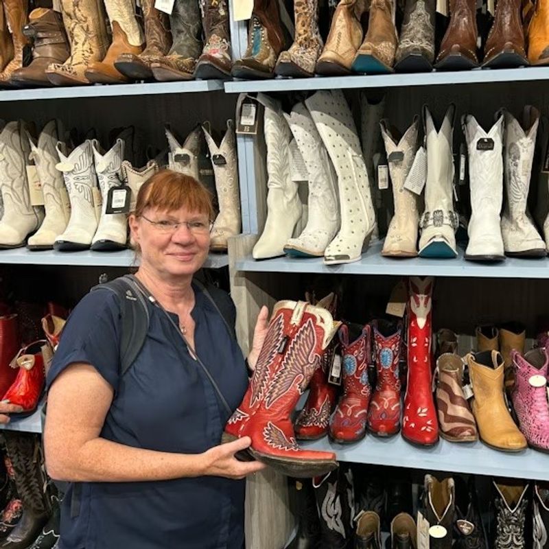 Frau steht vor Regal mit Cowboystiefeln und hält einen roten Stiefel in der Hand